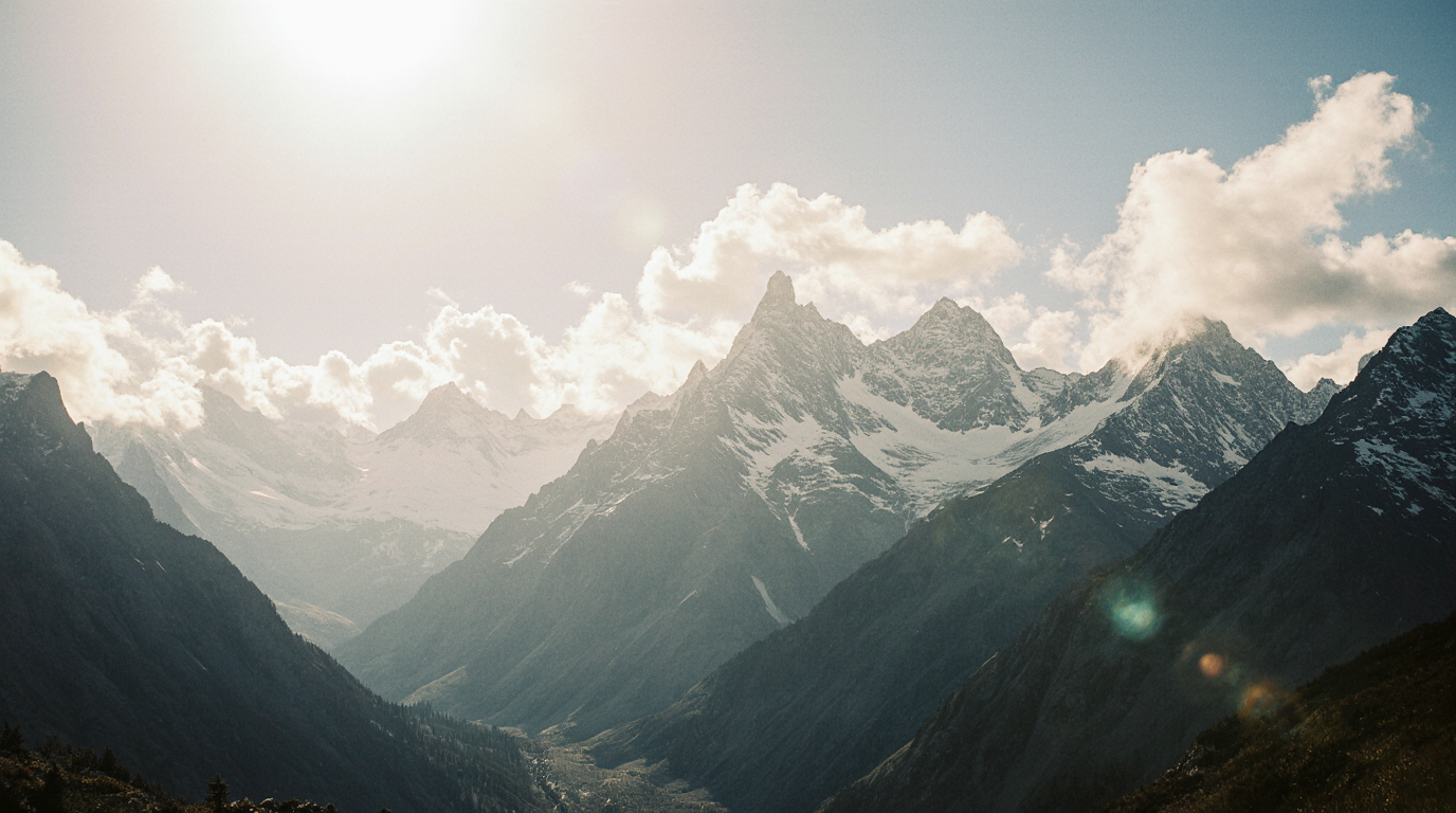 Snow-capped mountains with clouds and sunlight in a valley